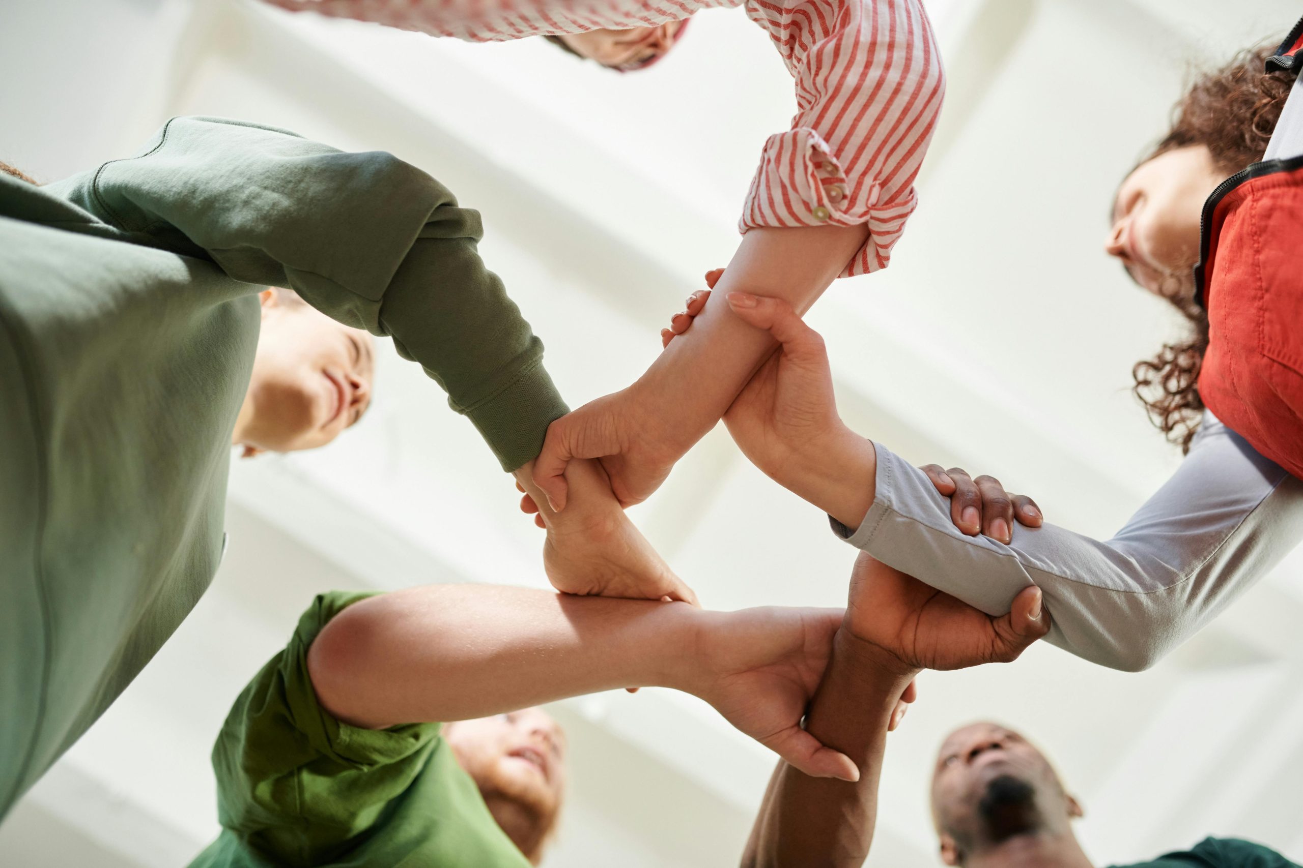 A diverse group of people join hands forming a unity circle, symbolizing teamwork and cooperation.